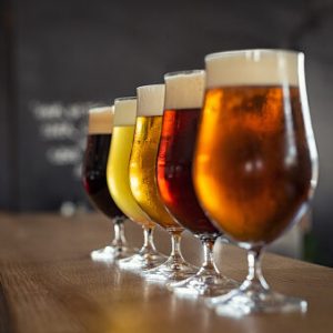 Glasses with different sorts of craft beer on wooden bar. Tap beer in pint glasses arranged in a row. Closeup of five glasses of different types of draught beer in a pub.
